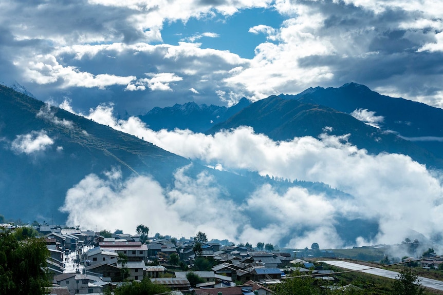 Mountains shrouded in clouds with a city in the foreground.
