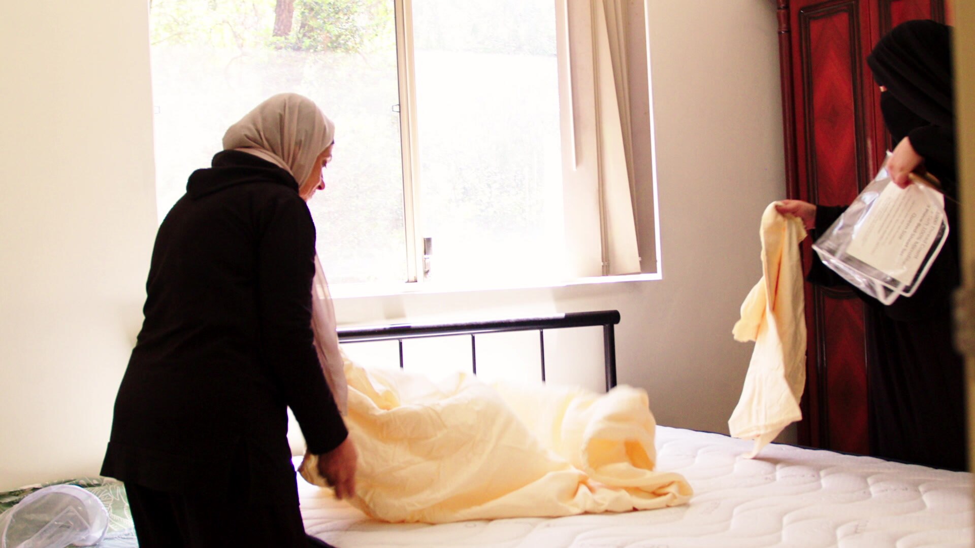 Umm Ali is making up the bed sheets of her brand new bed.