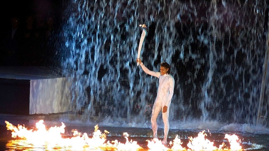 Freeman, standing in a ring of fire and a cascade of water, holds aloft the Olympic torch