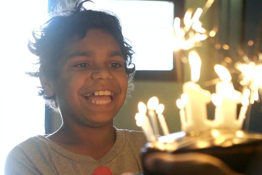 A boy smiles while holding a birthday cake with candles alight