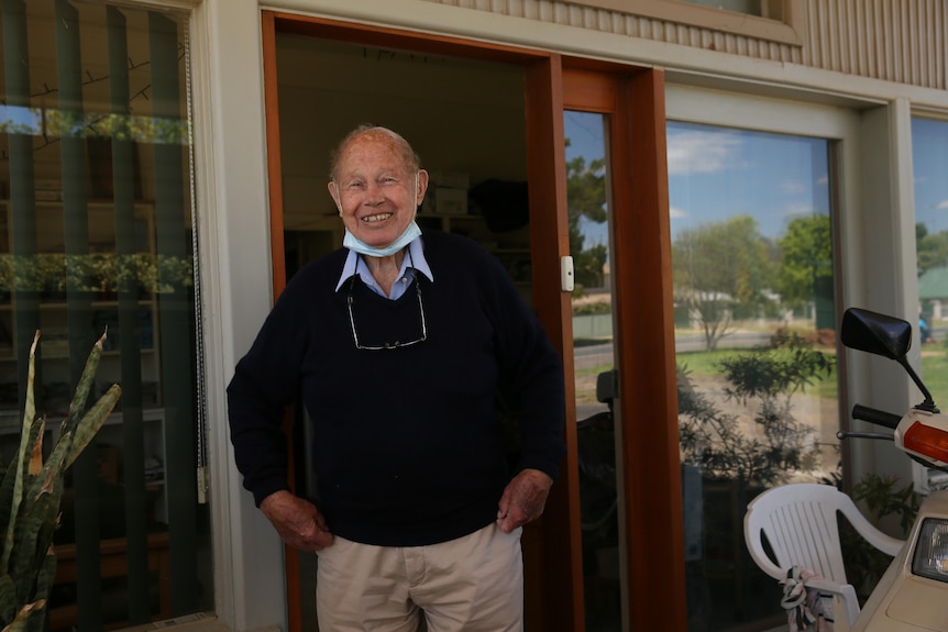 Un homme avec un pull souriant à une caméra