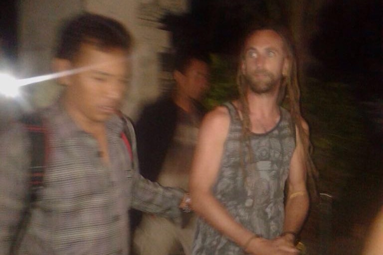 British man David Taylor wears handcuffs as he is led by a police officer