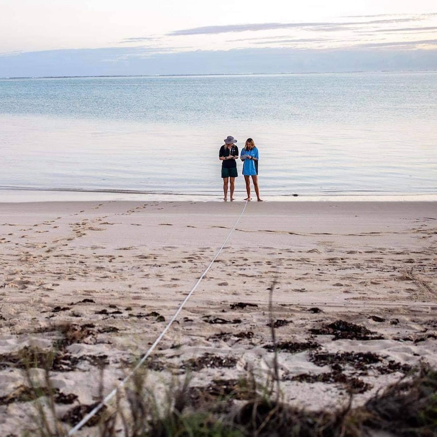 Two women stand on the beach next to the ocean, early in the morning so the colours are soft and pastel