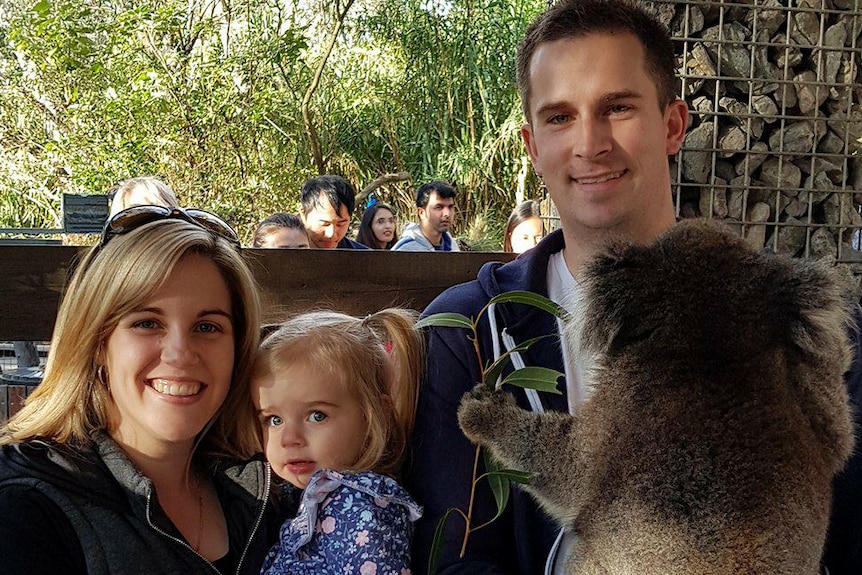 A man and woman stand holding a little girl and a koala.