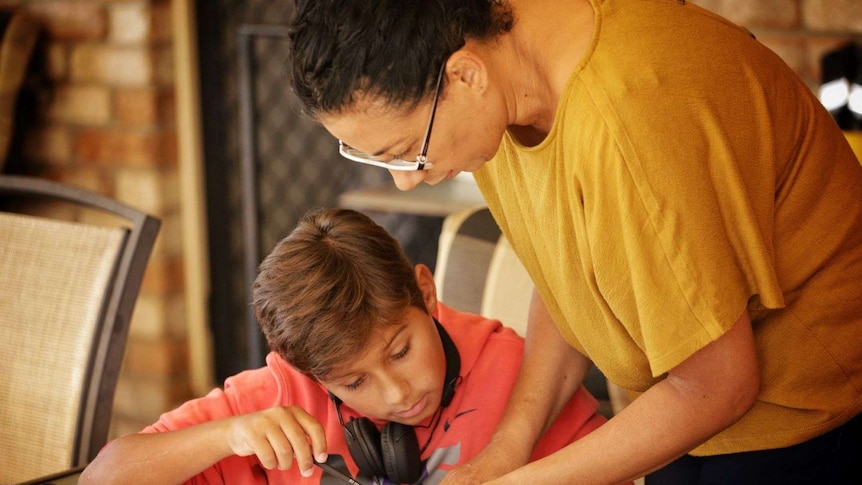 A woman stands over a son to help him with his school work