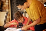 A woman stands over a son to help him with his school work