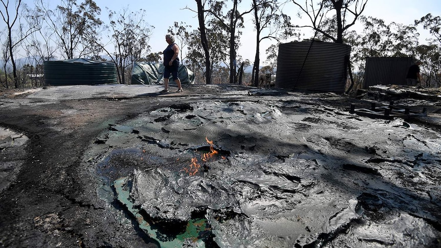 Resident Jeanette Schwindt inspects her melted water tanks after bushfires at her Mount Larcom property.