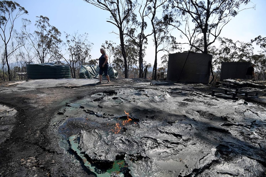 Resident Jeanette Schwindt inspects her melted water tanks after bushfires at her Mount Larcom property.