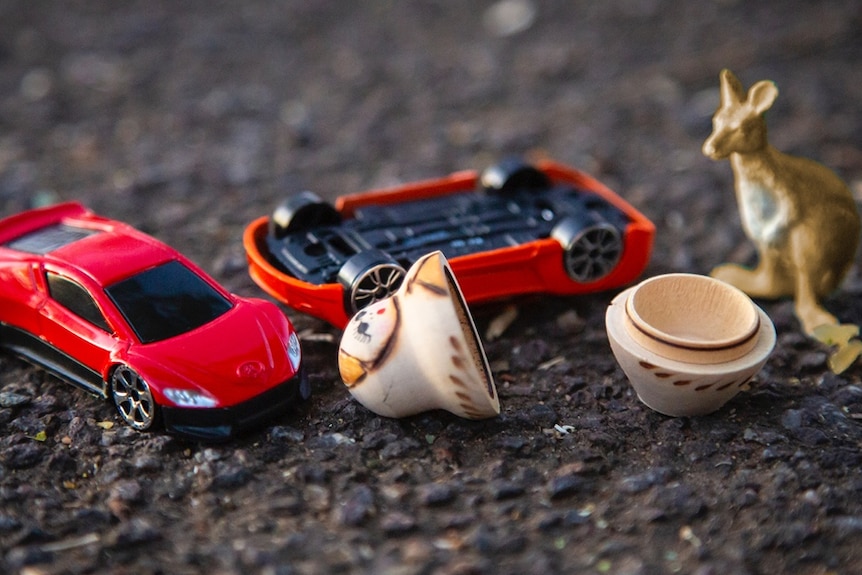Toy cars, a kangaroo and a babushka doll on asphalt.