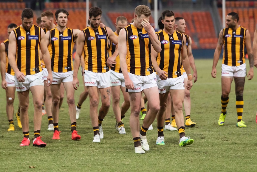 A group of AFL players walk off looking glum after losing a match.