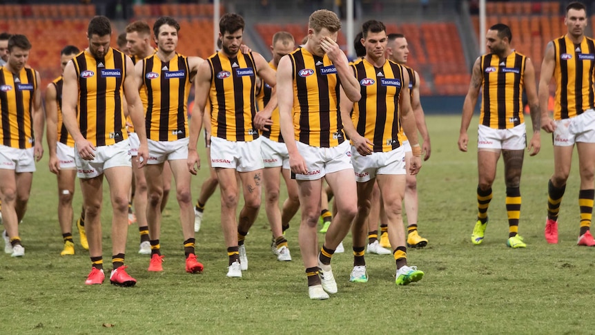 A group of AFL players walk off looking glum after losing a match.