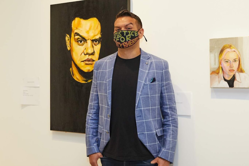 Young man in light-blue jacket posing with self-portrait, while wearing face mask that reads: Justice for Aunt Sherry.