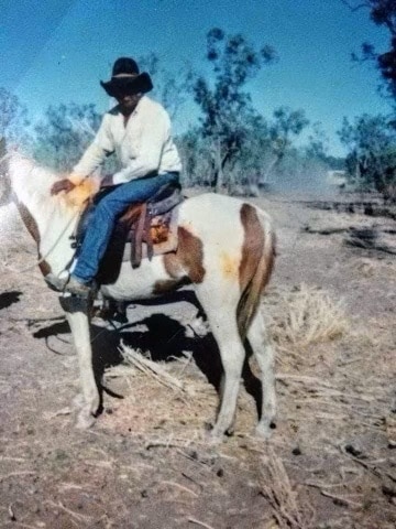 An Aboriginal man sits on a horse with a cowboy hay on. 