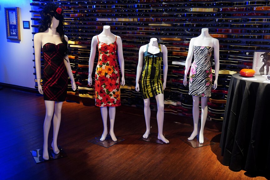 Four mannequins wearing different dresses are lined up. One is wearing a wig similar to Amy's iconic beehive hairstyle.