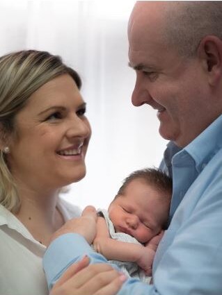 A newborn baby cradled between his smiling parents.