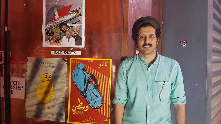 Saudi filmmaker Ali Kalthami stands next to the poster for his film "Wasati" or "Moderate".