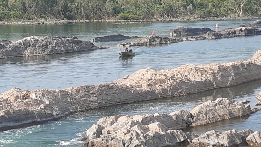 A boat cruises in water between rock bars