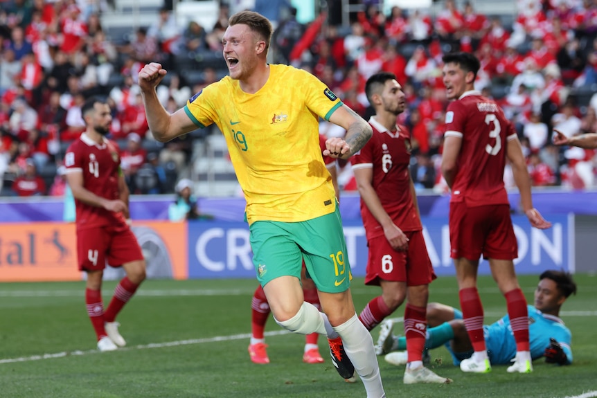 A soccer player wearing yellow and green celebrates after scoring a goal against a team in red and white