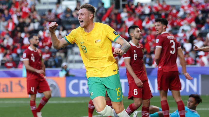 A soccer player wearing yellow and green celebrates after scoring a goal against a team in red and white