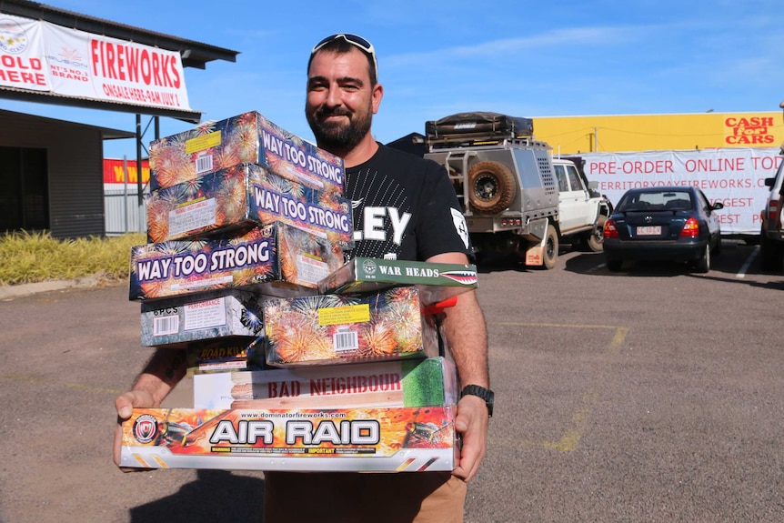 A man with a tall stack of fireworks boxes