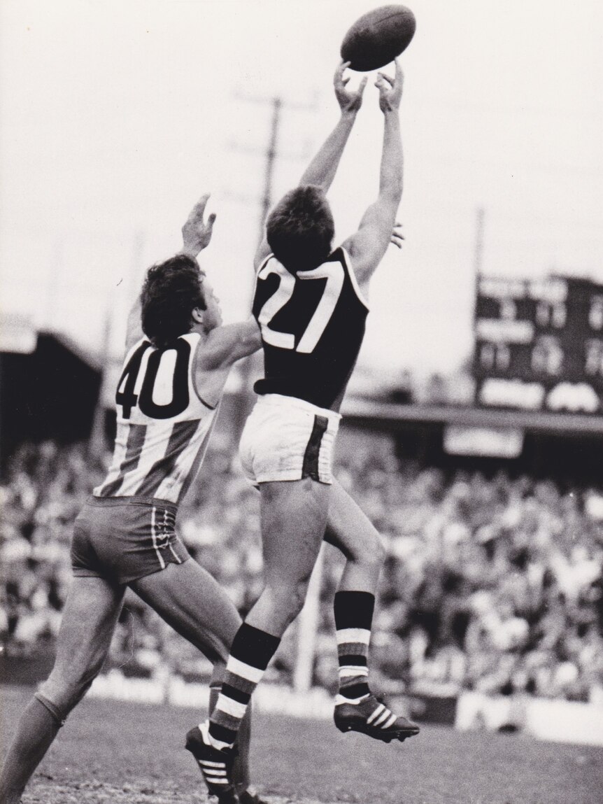 An Australian rules player jumps for a mark, the ball at his fingertips.