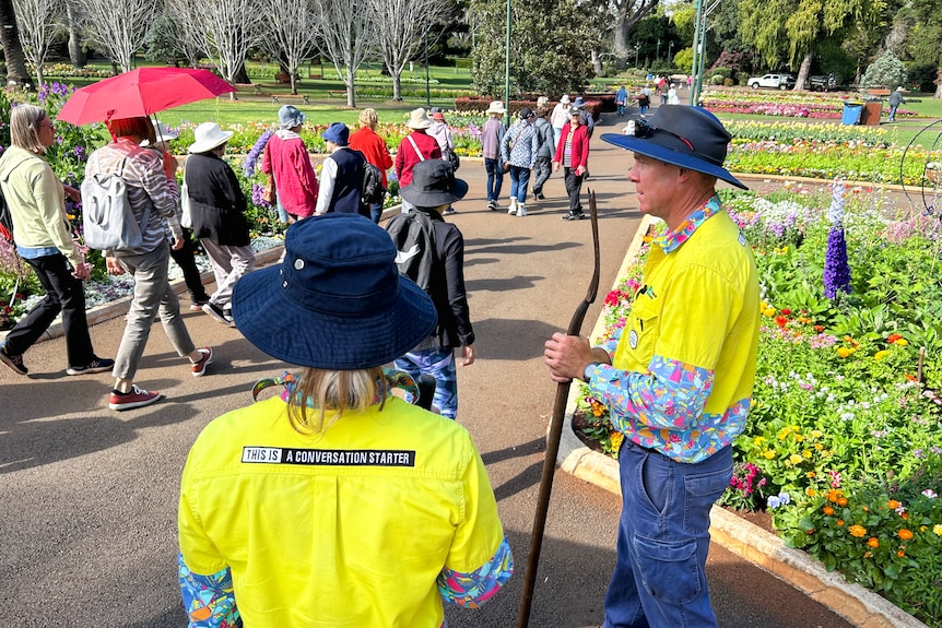 Two gardeners watch a group of tourists walk through a park