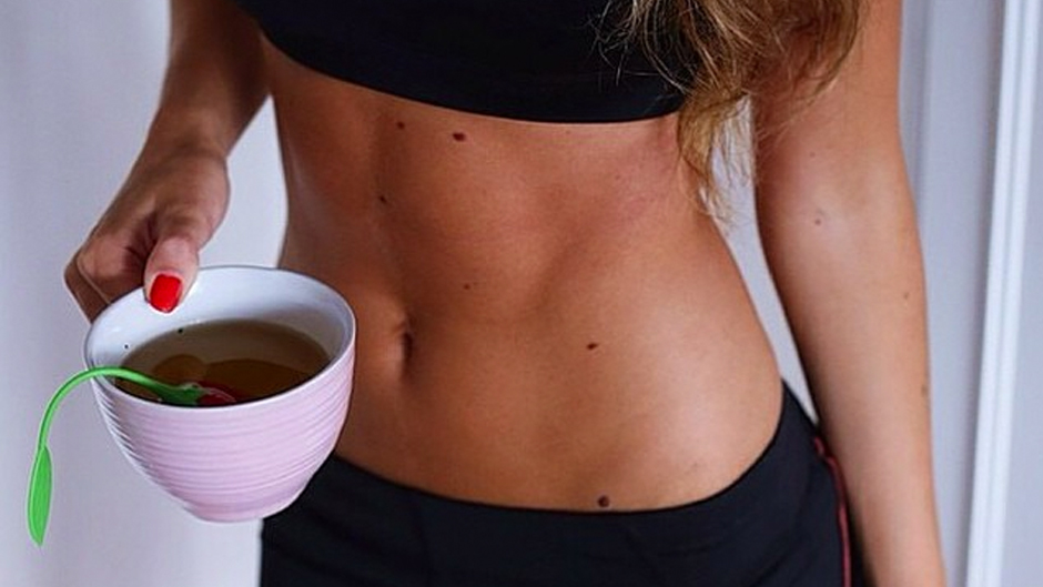A woman holds a mug of detox tea near her stomach.