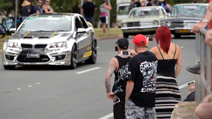 People photograph a parade of cars making their way down Northbourne Avenue in Canberra.