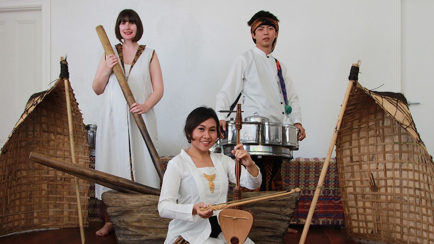 Bianca Gannon holds a timber rod, Luqmanul Chakim holds a large silver tin and Peni Candra Rini holds a timber string instrument