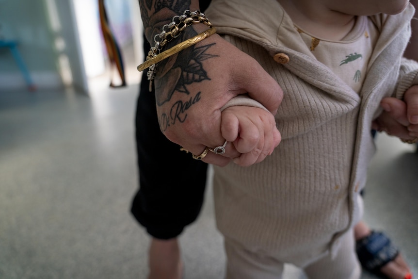 A woman holds a baby's hand