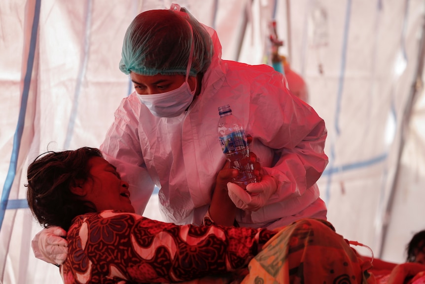 A healthcare worker in PPE treats patient inside a tent erected outside an emergency ward in Indonesia