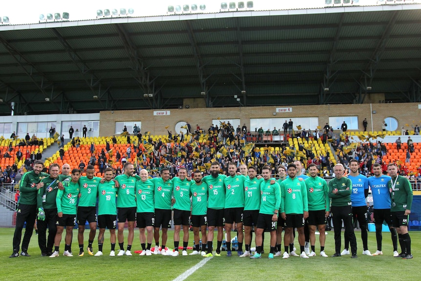 The Socceroos squad links arm with supporters in the background at training