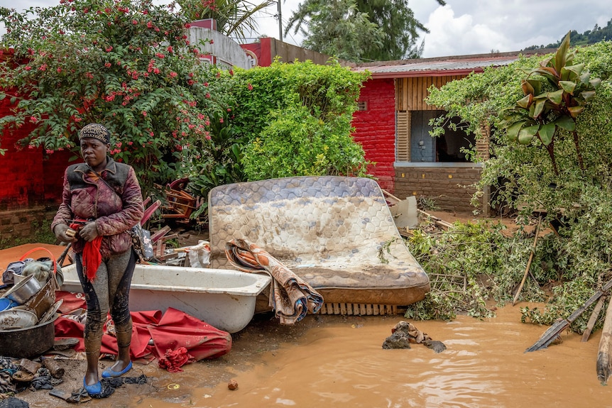 A woman stands in flood water next to debris. 
