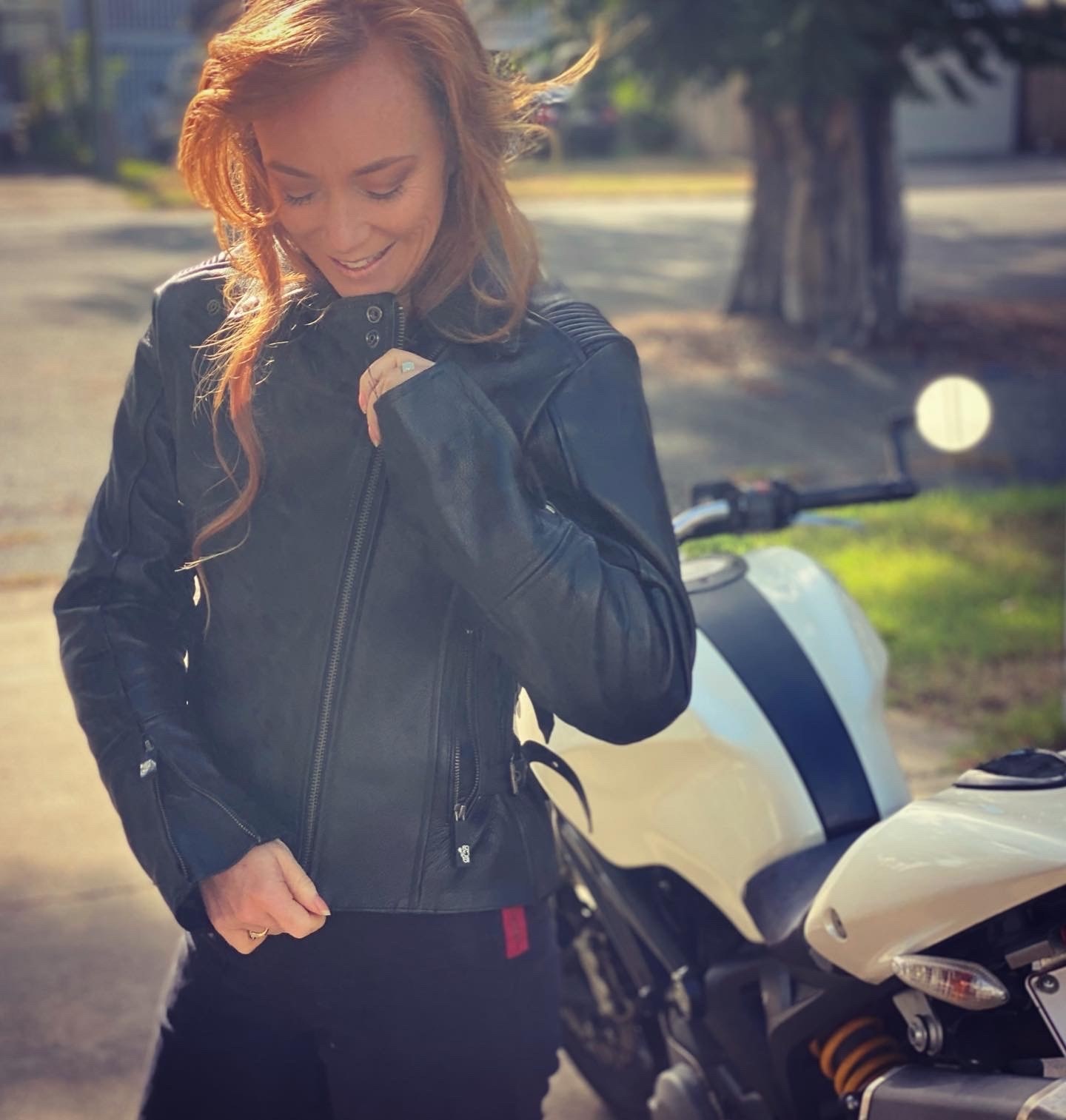 A woman with long red head zips up a leather biking jacket.