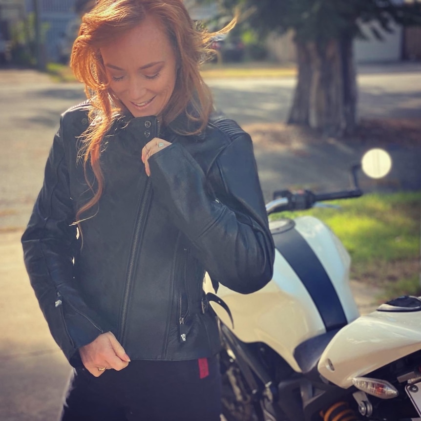 A woman with long red head zips up a leather biking jacket.