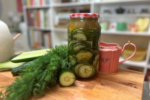 A jar of pickled cucumbers sits on a chopping board.