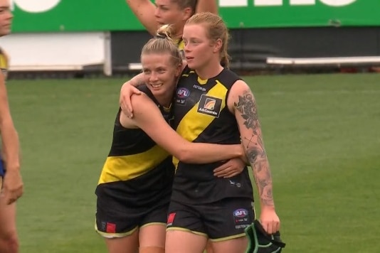 Two players in black singlets with a yellow sash hug each other