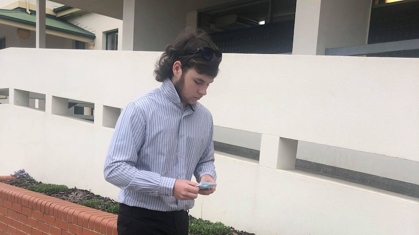 Blake William Banner wearing a blue button up shirt and sunnies on his head. He has a mullet. 