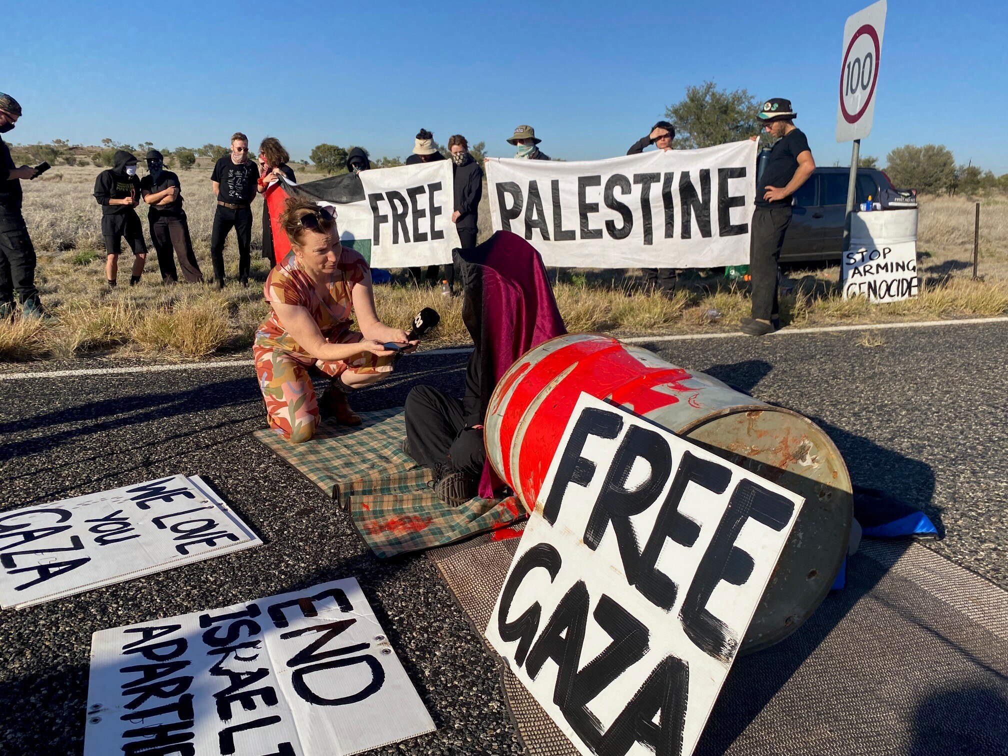 A group of people block a road through the outback with signs saying 'free Gaza'. 
