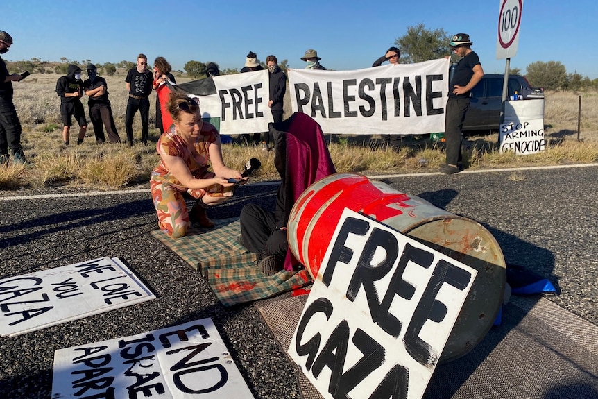 A group of people block a road through the outback with signs saying 'free Gaza'. 