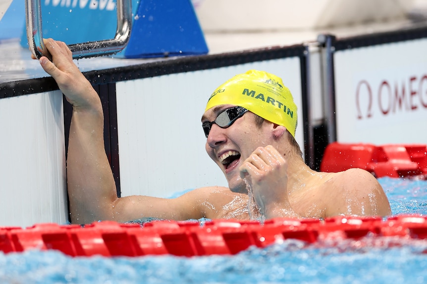 A smiling Australian Paralympic swimmer celebrates in the water after winning a gold medal in Tokyo. 
