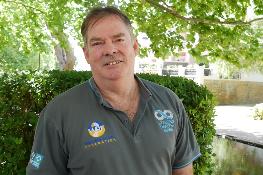 A man with short, dark hair, wearing a branded polo shirt, stands outside, smiling.