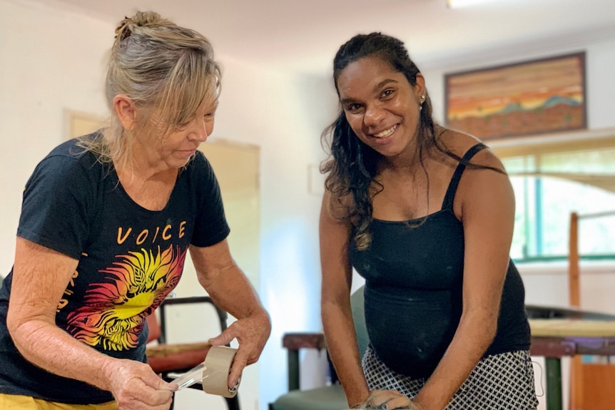 An older woman stands next to a younger Aboriginal woman as they do screen-printing at a table.