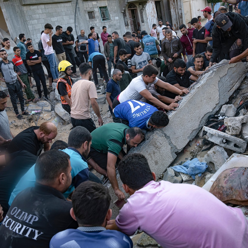 A crowd of people search desperately through a collapse building and rubble in the street