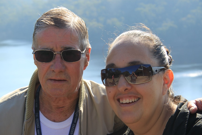 An elderly man puts his arm around a younger woman.