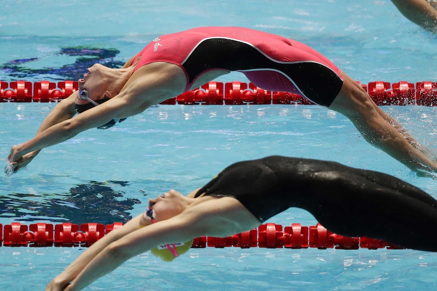 Two women jump drive backwards into a pool side by side.