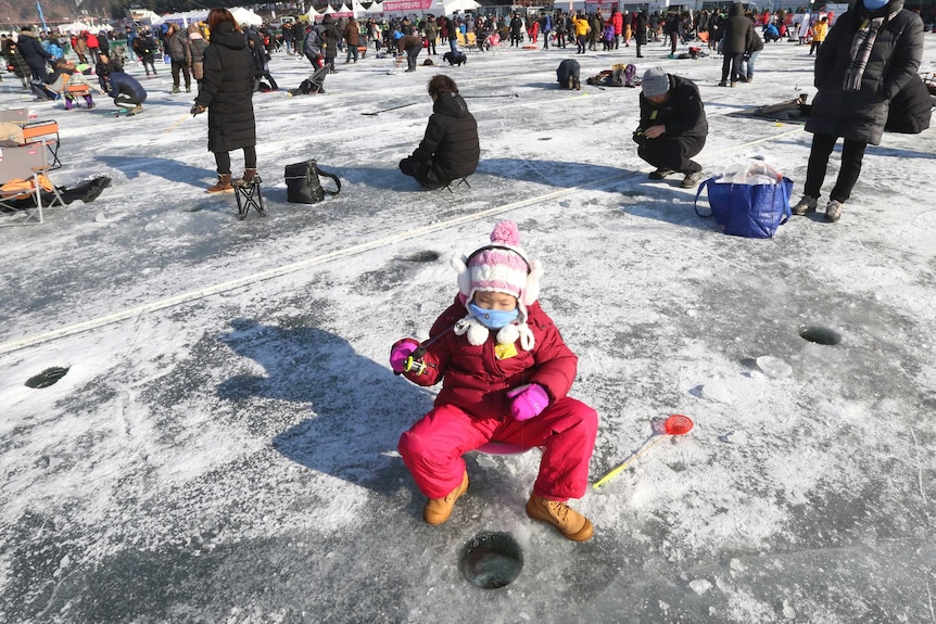 A girl casts a line through a hole drilled in the surface of a frozen river