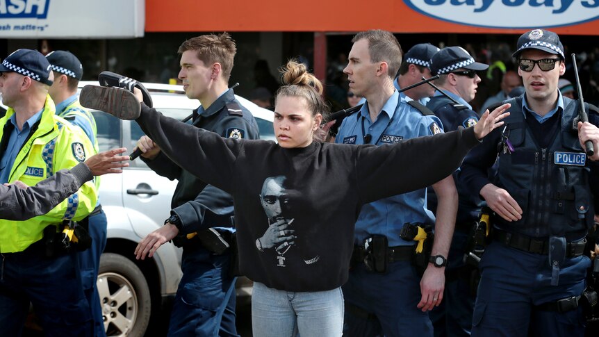 Hayley Garlett stands in front of police with arms outstretched.