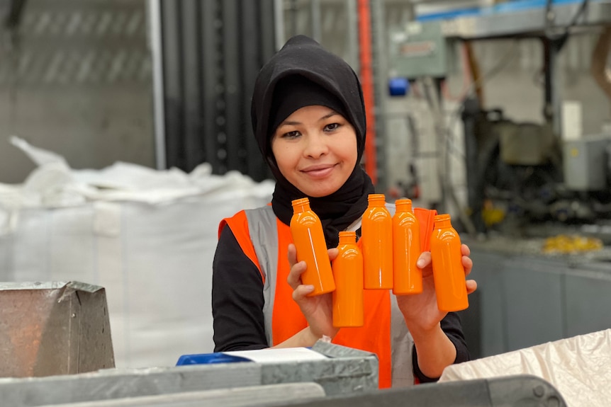 Female migrant worker pictured in orange hi vis vest and holding orange plastic bottles.