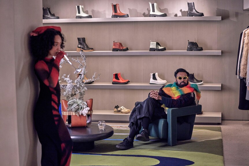 A film still of Ruth Negga and Himesh Patel in a fancy shoe store. Negga stands against a wall, drinking champagne.